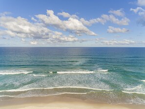 Una playa con olas, cielo despejado y nubes.