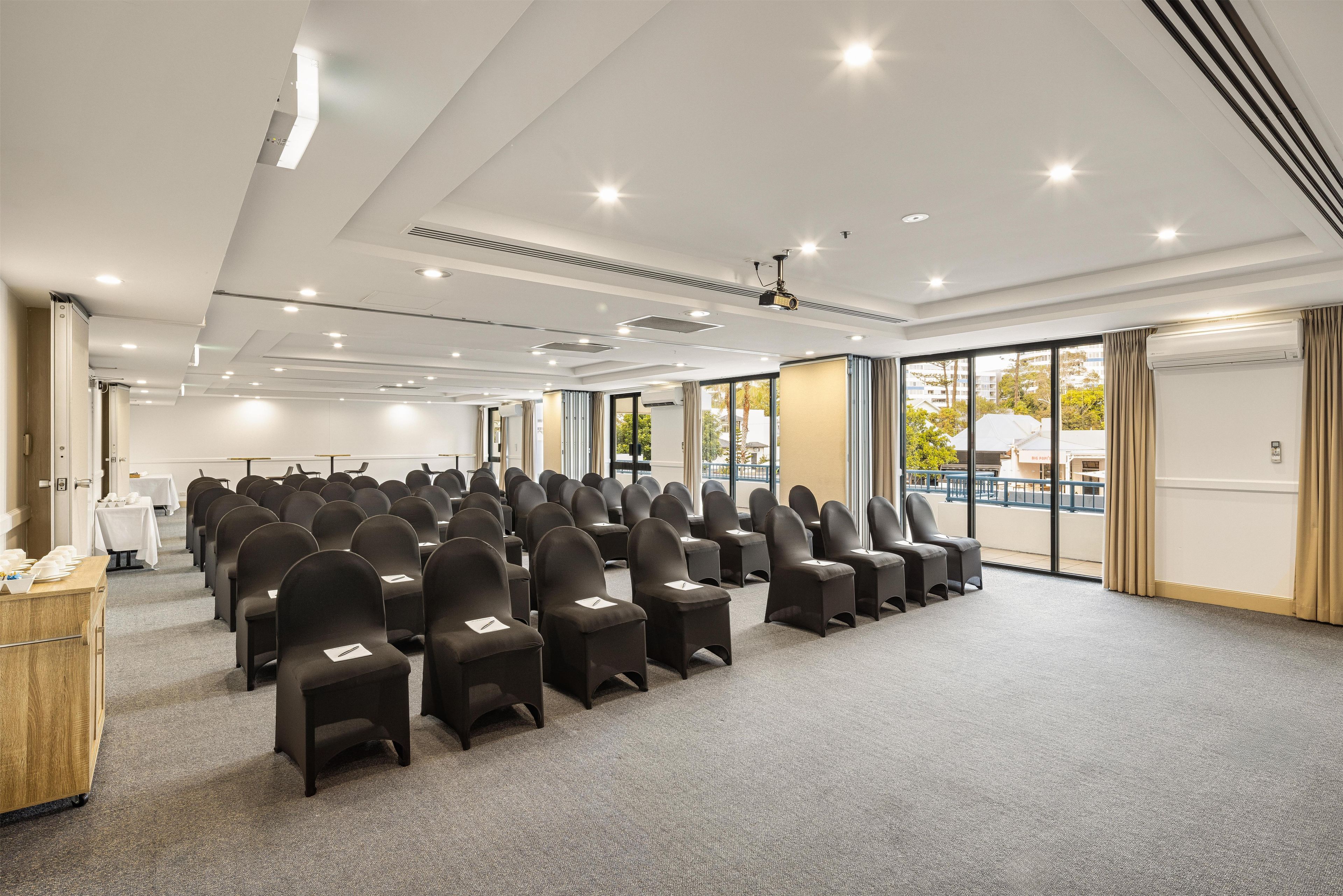 Un salón de conferencias con filas de sillas, un atril y un amplio ventanal con vista a edificios.