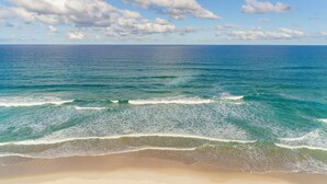A beach with clear blue water and white waves, a sandy shore, and a partly cloudy sky.