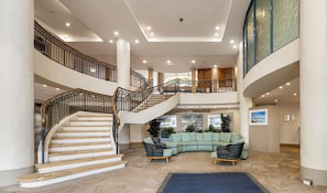 A spacious lobby with a central staircase, a curved seating area, and a second-floor balcony.