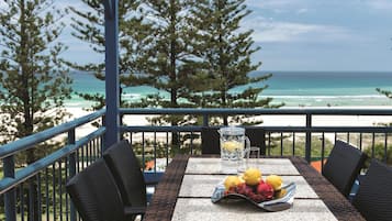 A balcony with a table set for two, overlooking a beach and ocean.