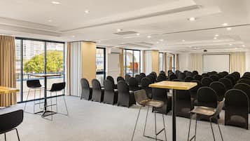 A conference room with rows of chairs, tables, and a large window with curtains.