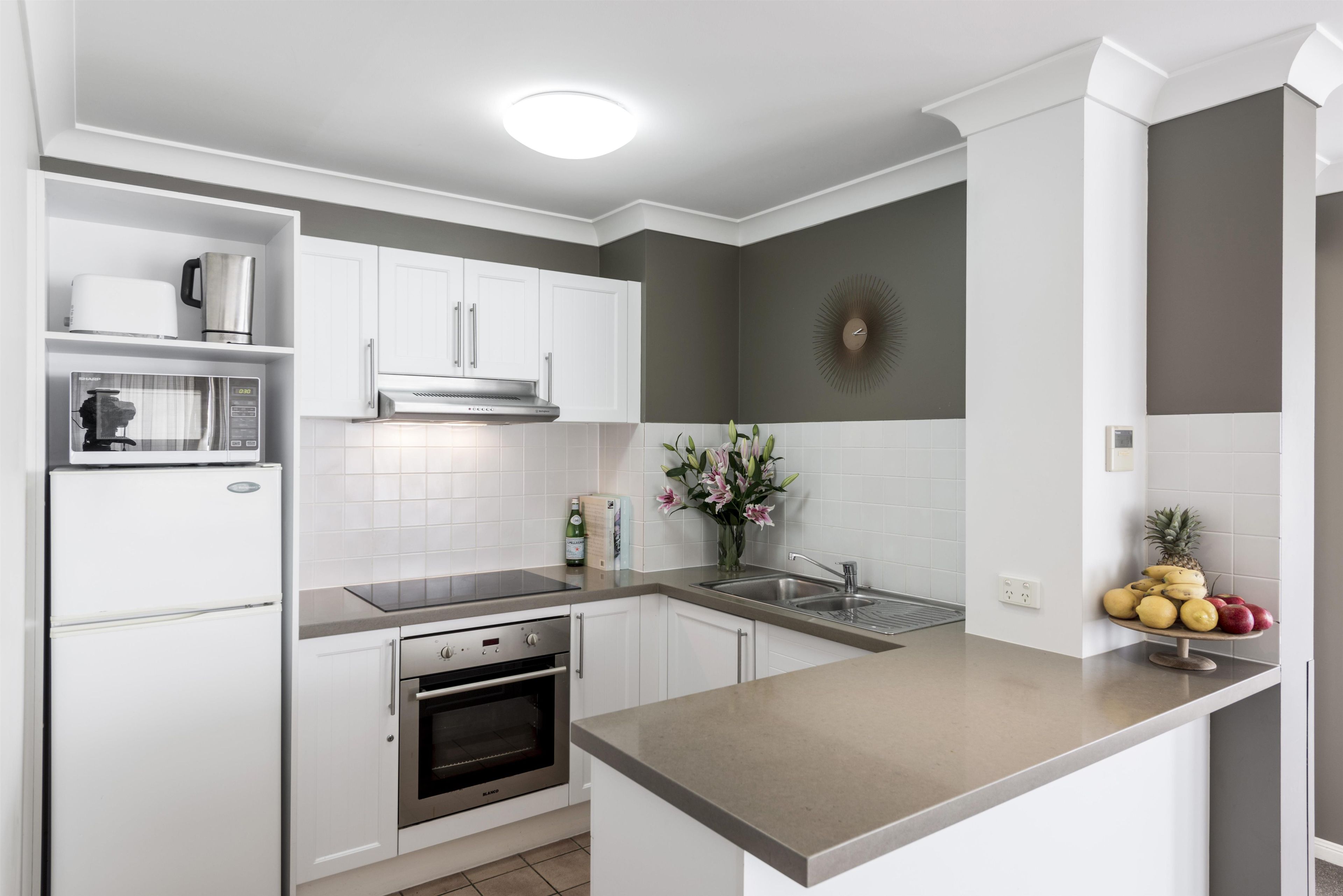 Una cocina moderna con armarios blancos, horno empotrado, campana de acero inoxidable y encimera de granito.