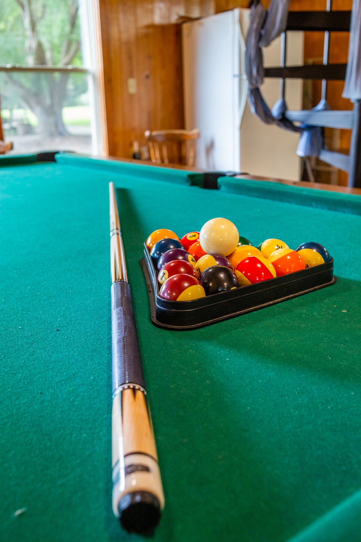 A pool table with a cue stick and a rack of billiard balls.
