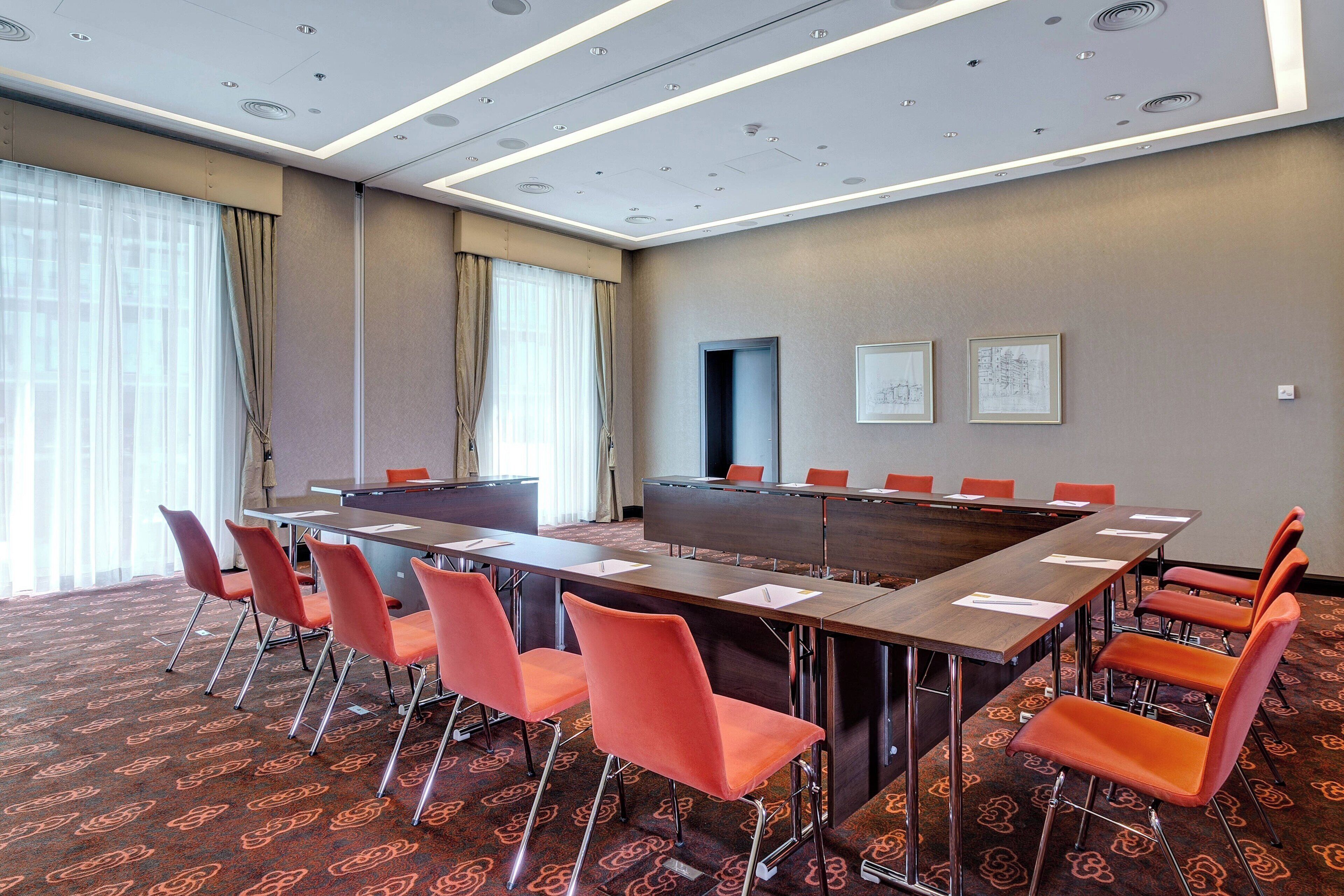 A conference room with a long table, orange chairs, and a patterned carpet.