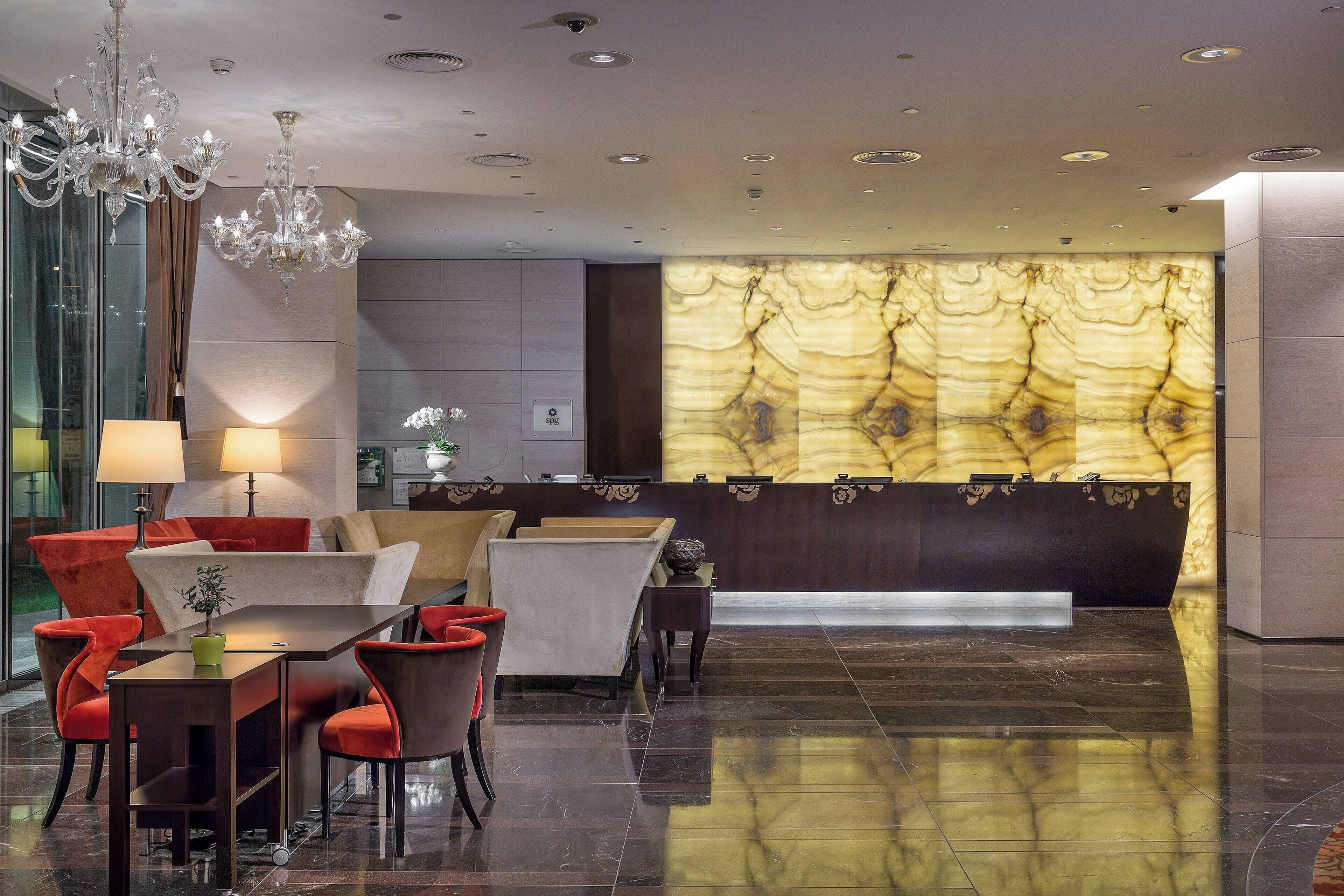Een moderne hotel lobby met een receptiebalie, een zithoek en een kroonluchter.