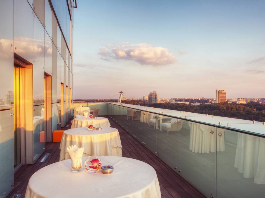 A rooftop terrace with tables set for dining, overlooking a cityscape with buildings and a tower.