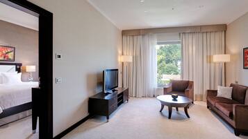 A hotel room with a bed, a TV on a stand, a sofa, a coffee table, and a window with curtains.