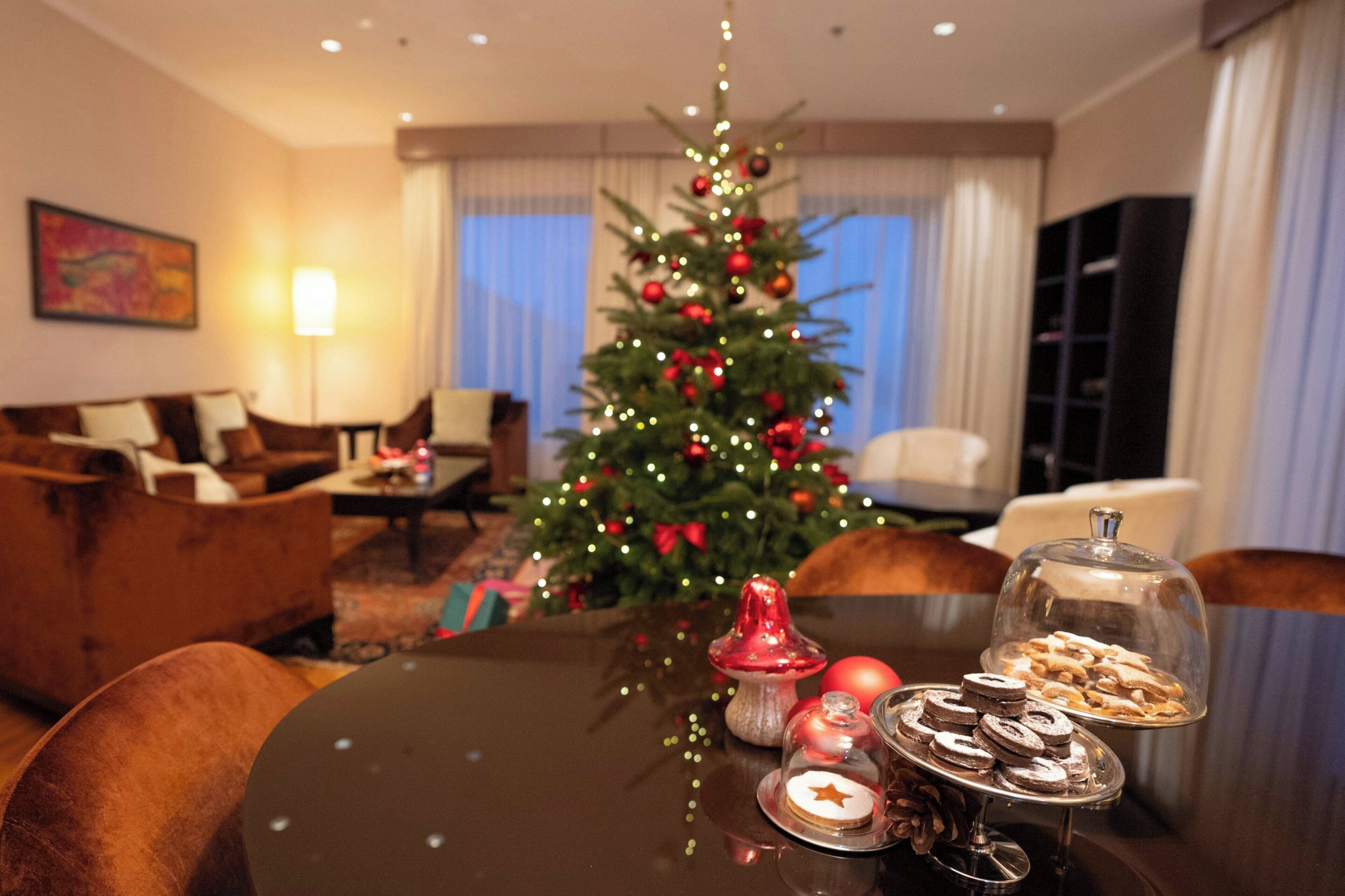 Una mesa de comedor con un árbol de Navidad, una lámpara y una presentación de postres en una habitación de hotel.