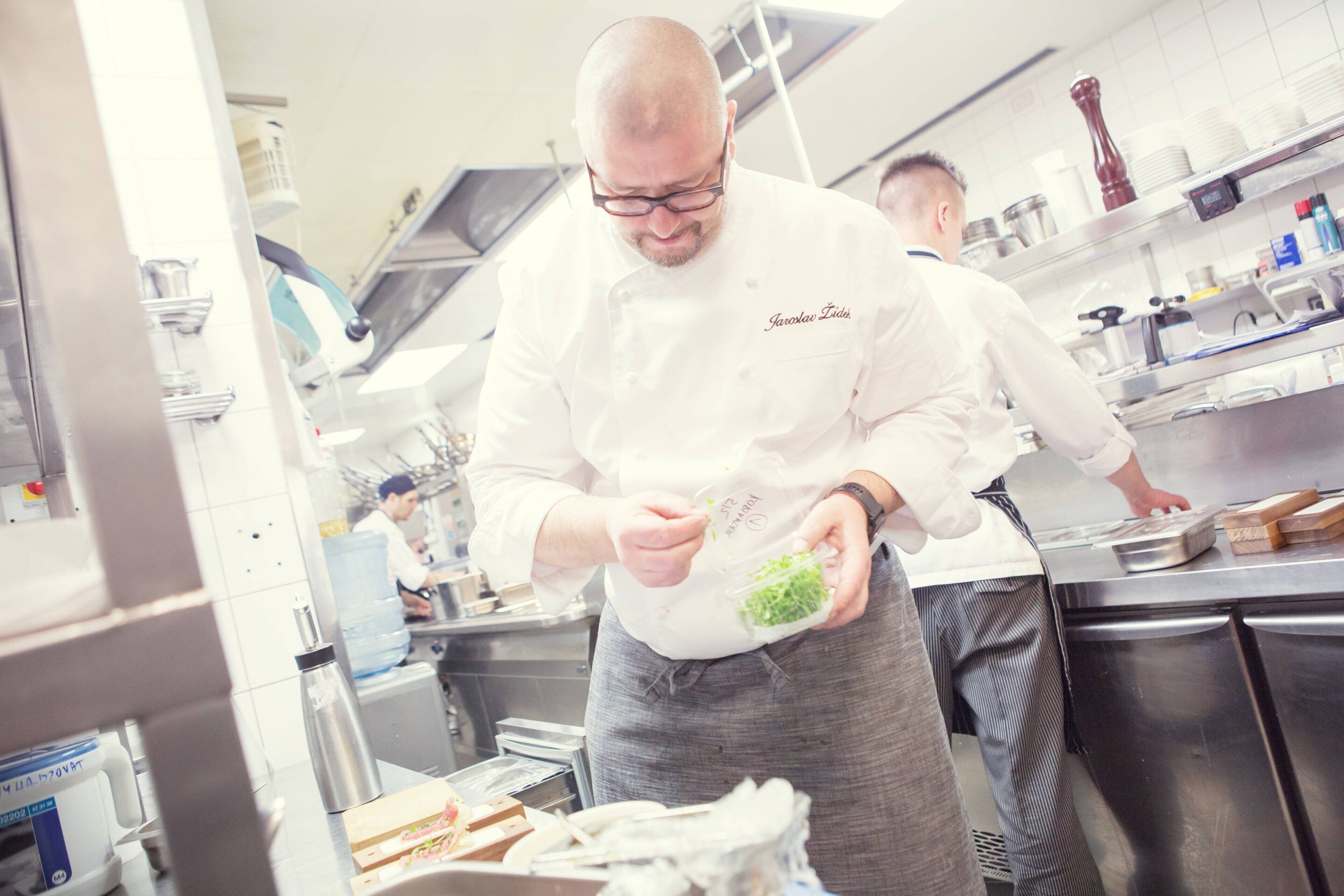 A chef preparing food in a professional kitchen with stainless steel appliances and a water dispenser.