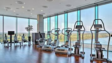 A gym with cardio machines, a TV, and large windows with a view of a river.