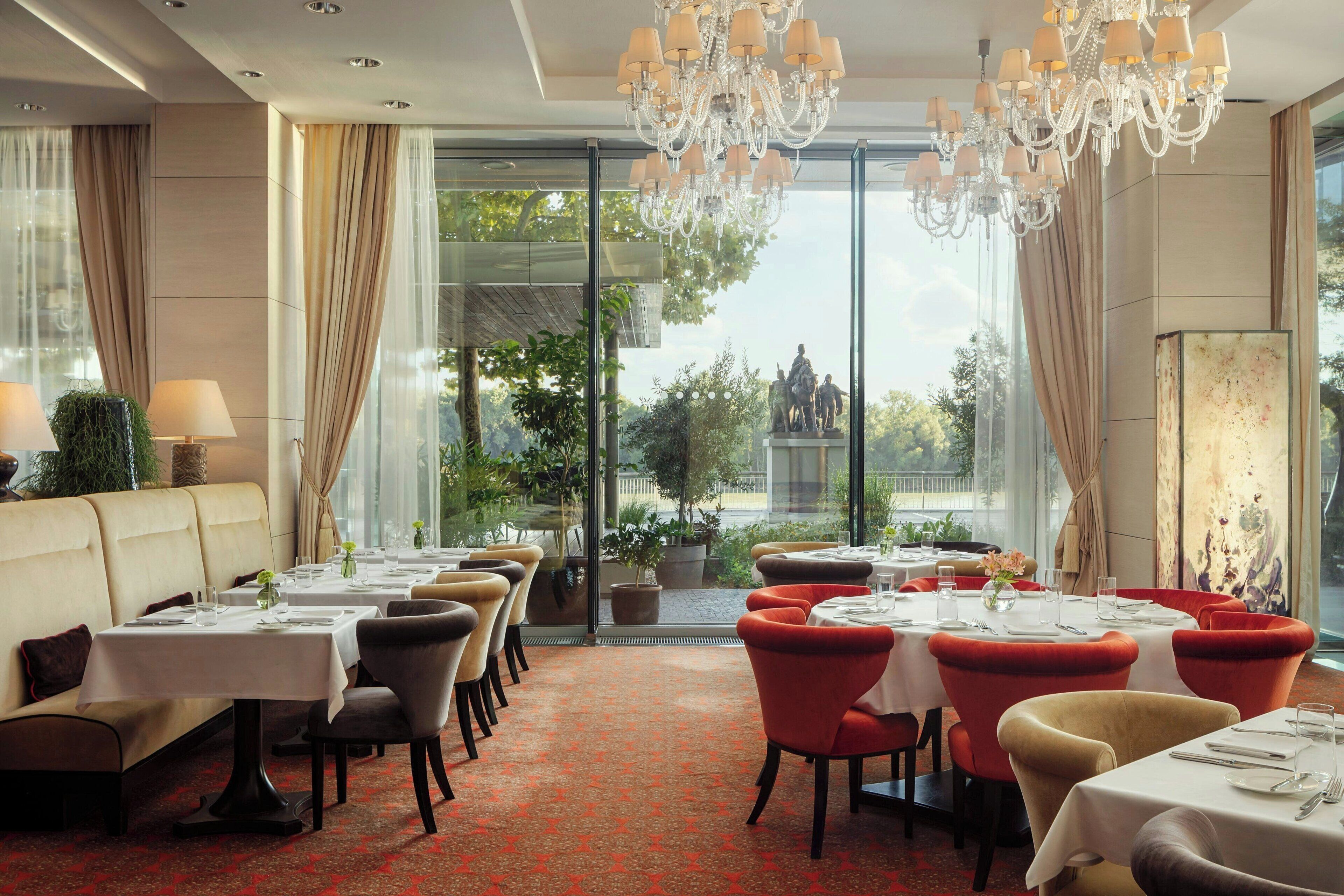 A restaurant with tables set for dining, a chandelier, and a view of the outdoors.