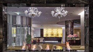 Een moderne lobby met een marmeren receptiebalie, een zithoek met een open haard en een kroonluchter.