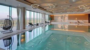 Ein moderner, überdachter Pool mit gläsernem Boden, großen Fenstern mit Landschaftsblick und zeitgemäßer Beleuchtung.