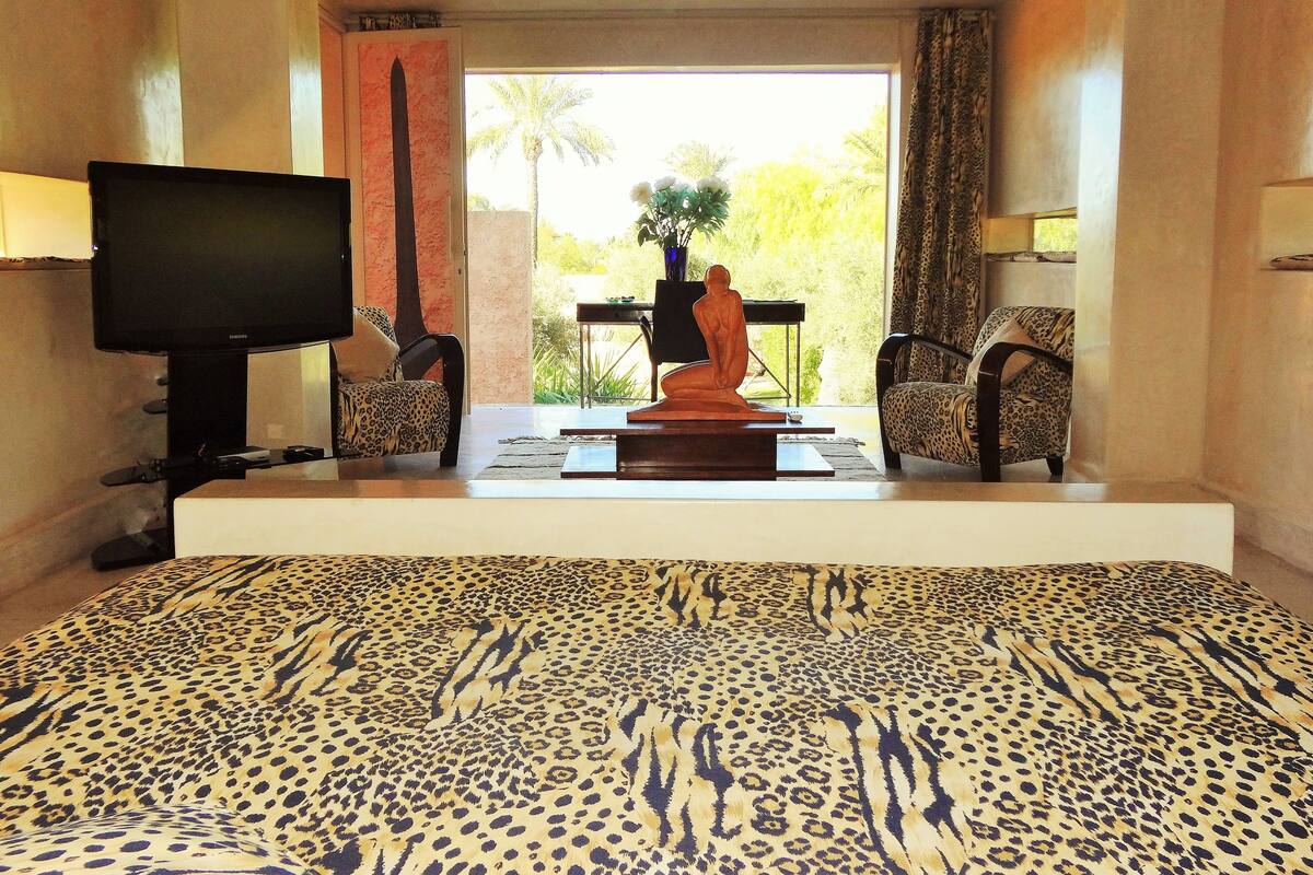A hotel room with a large bed, a television, a statue, and a view of palm trees.