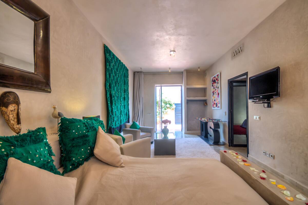 A hotel room with a bed, a sofa, a television, and a large mirror.
