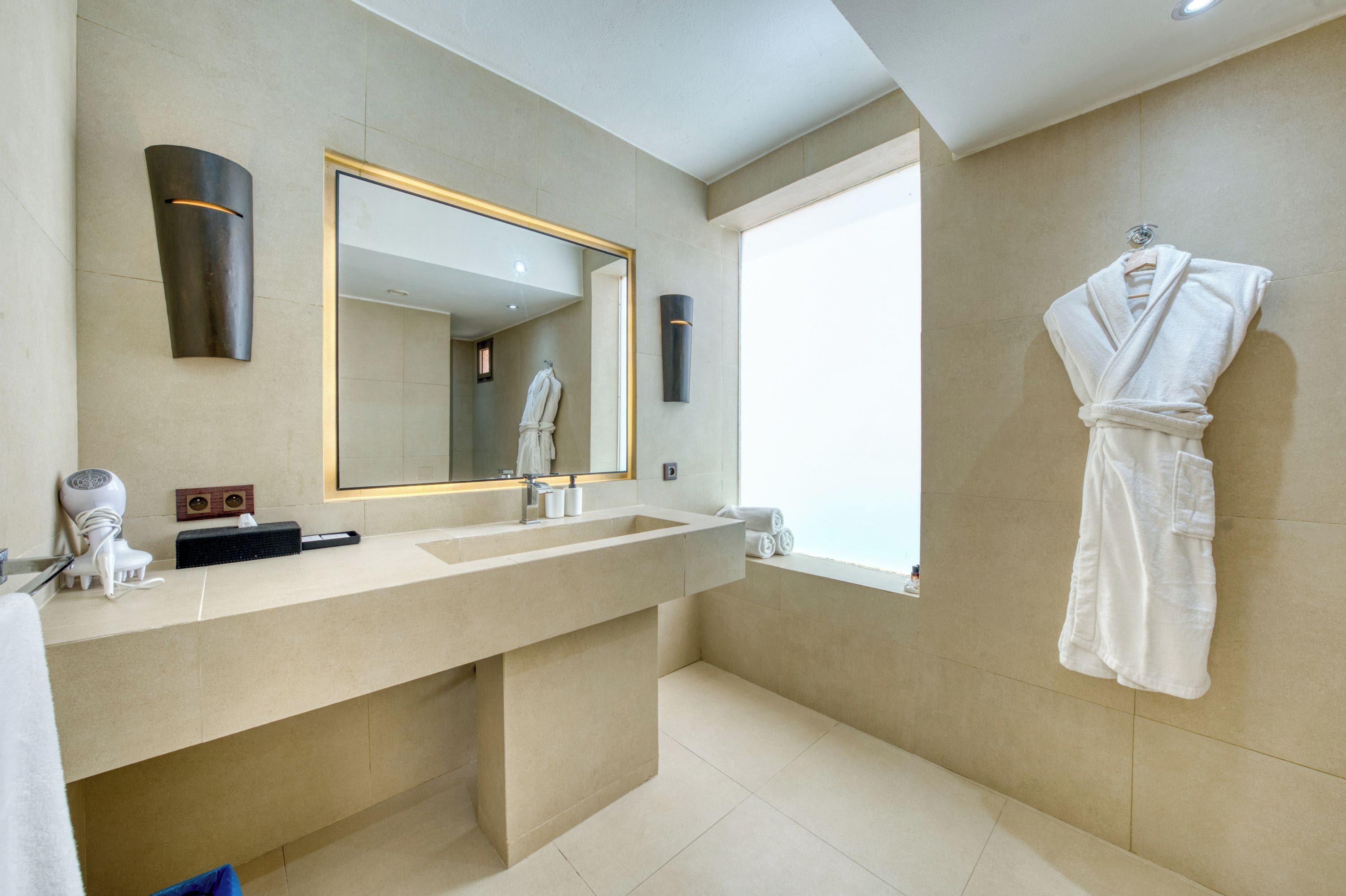 A modern bathroom with a large mirror, a vanity with a sink, and a robe hanging on the wall.