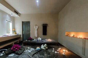 Un cuarto de spa con dos camillas de masaje, un tocador con espejo y un estante con velas.