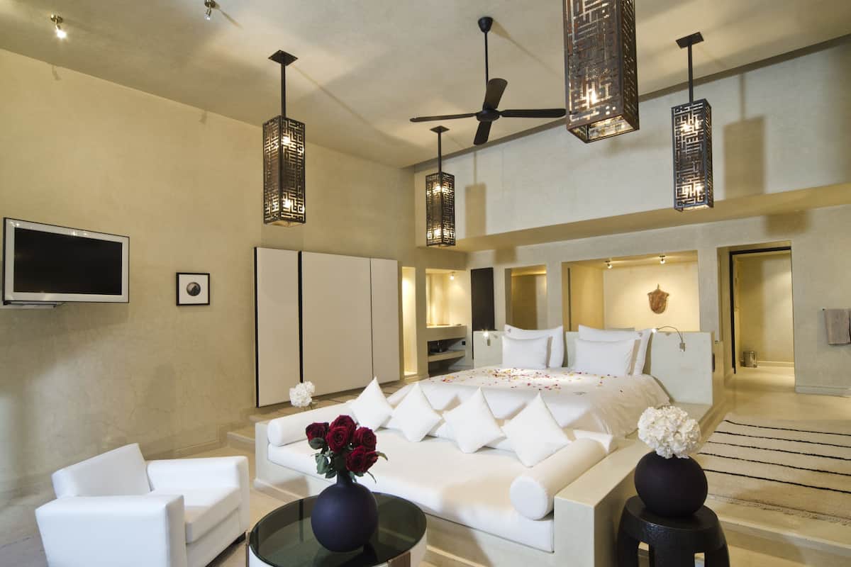 A modern hotel room with a large bed, white furniture, a TV, and decorative lighting.