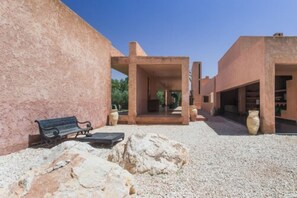 A courtyard with a bench, large vases, and a building with open spaces. - Hôtel Dar Sabra (Marrakech)