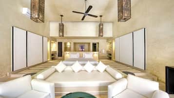 A spacious bedroom with a large bed, two white sofas, a ceiling fan, and decorative lighting fixtures.