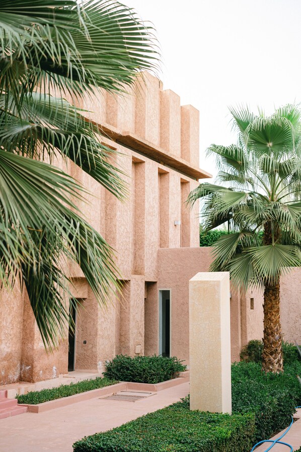 Un edificio de fachada color beige, palmeras y un jardín bien cuidado.