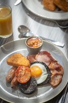 A breakfast plate with eggs, bacon, sausages, a grilled tomato, and beans.