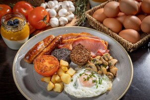 Ein Frühstücksteller mit Würstchen, Speck, Eiern, Pilzen und Tomaten.