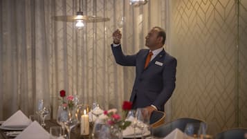 A man in a suit serving a glass of wine at a table set with candles and flowers.