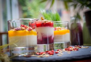 Drei Schichtdesserts in klaren Gläsern, verziert mit Nüssen und Beeren, auf einer dunklen Oberfläche mit verstreuten Nüssen und Beeren rundherum.
