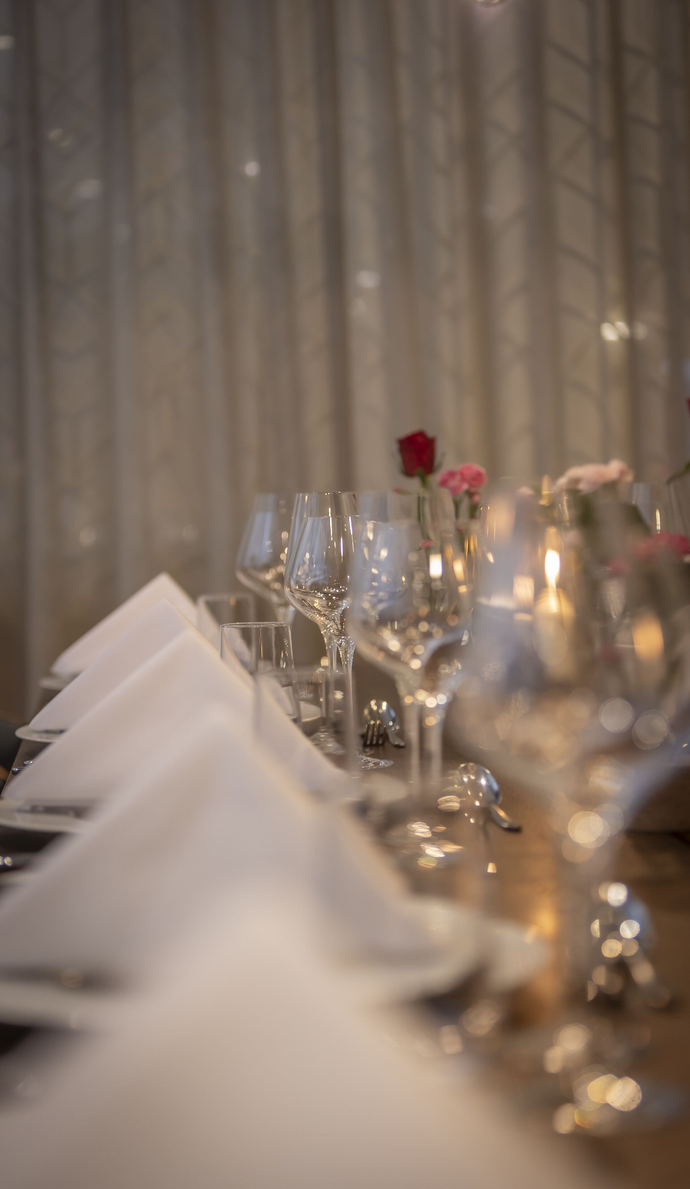 A table set with multiple wine glasses and a rose in a vase.