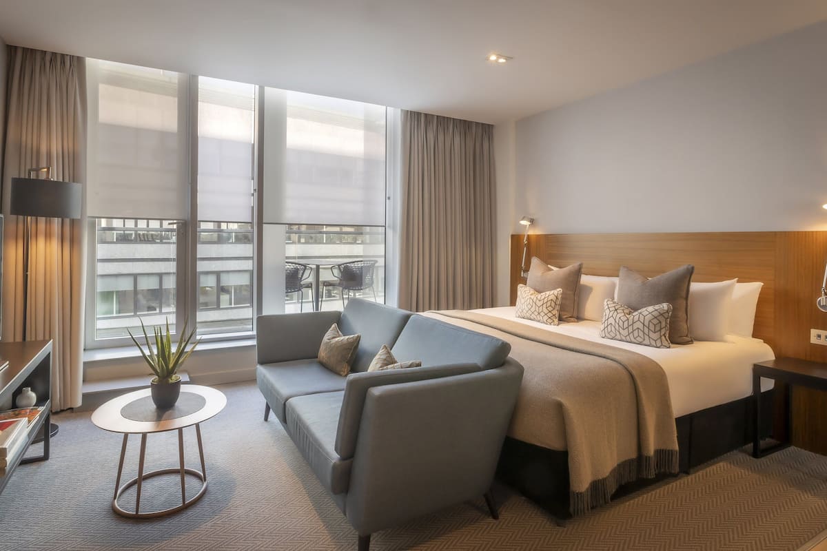 A modern hotel room with a large bed, a sofa, a TV, and a balcony with a view.