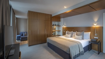 A modern hotel room with a large bed, wooden wardrobe, bedside tables, and a desk.