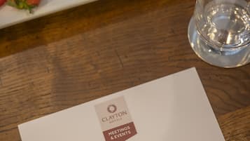 A plate of fruit and a glass of water on a wooden table with a hotel meeting and events brochure.