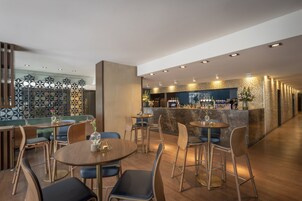 Ein modernes Restaurant mit runden Tischen und Barplätzen, einer Wand mit Muster und einer Bar mit einer Theke und verschiedenen Flaschen.