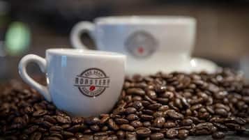 Two white ceramic coffee cups with the text "Hand Roasted" on them, surrounded by coffee beans.