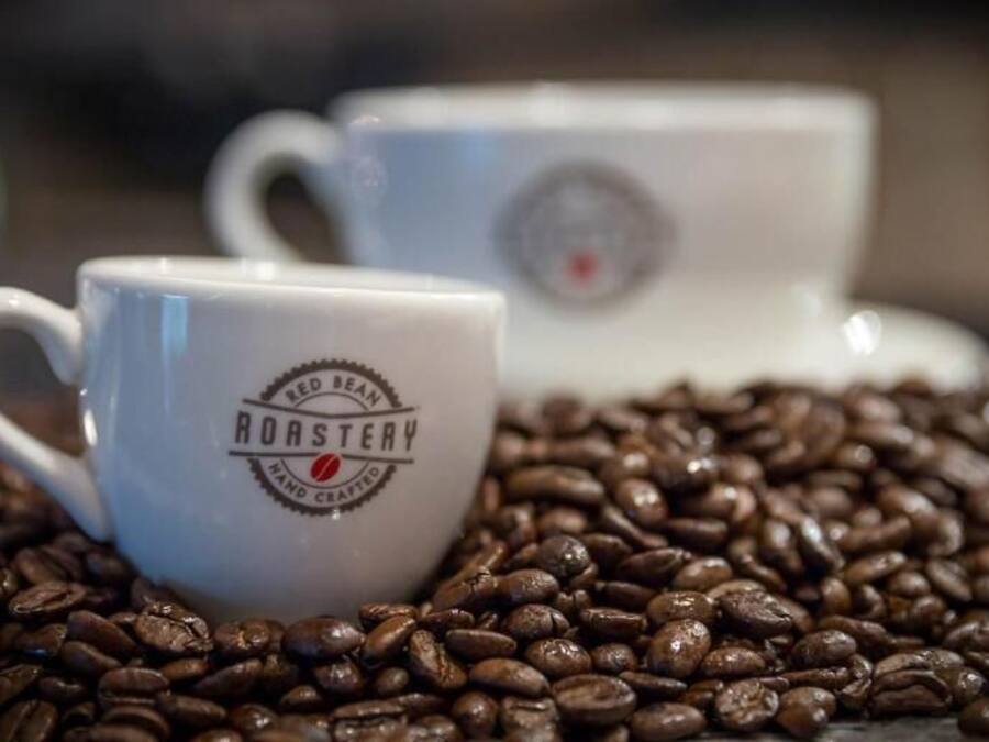Two white ceramic coffee cups with the text "Hand Roasted" on them, surrounded by coffee beans.