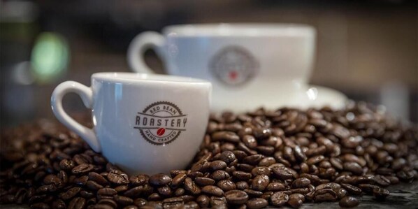 Two white ceramic coffee cups with the text "Hand Roasted" on them, surrounded by coffee beans.