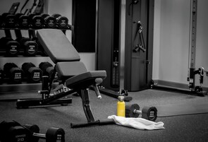 Ein Fitnessraum mit einer Bank, Kurzhanteln und einer Wasserflasche auf dem Boden.
