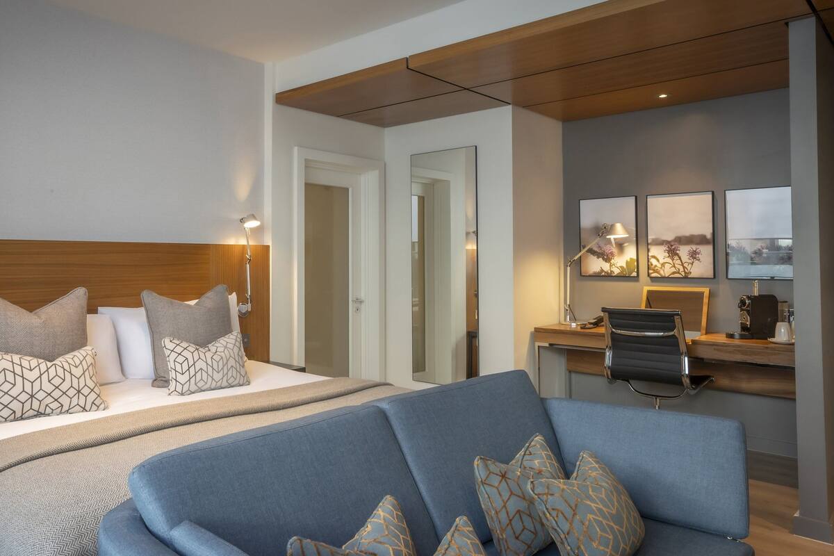 A hotel room with a bed, a desk, a chair, and a sofa.