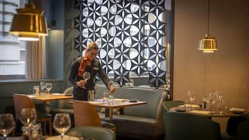 Interior de restaurante con un diseño moderno de pared geométrica, mesas de madera y asientos tapizados en verde.