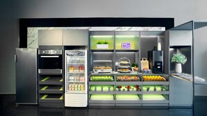 Moderni, itsepalveluperiaatteella toimiva aamiaisbuffet, jossa on kylmälaitteilla varustetut vitriinit, kahvinkeitin sekä valikoima tuoreita hedelmiä ja leivonnaisia.