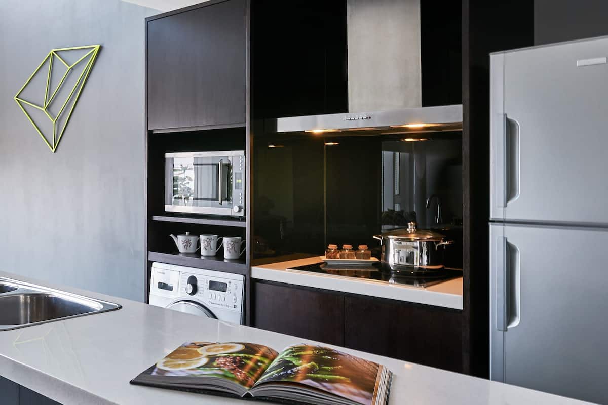 Une cuisine moderne équipée d’un four à micro-ondes, d’un four et d’un réfrigérateur encastrés. On peut voir un livre sur le comptoir et un élément décoratif géométrique accroché au mur.