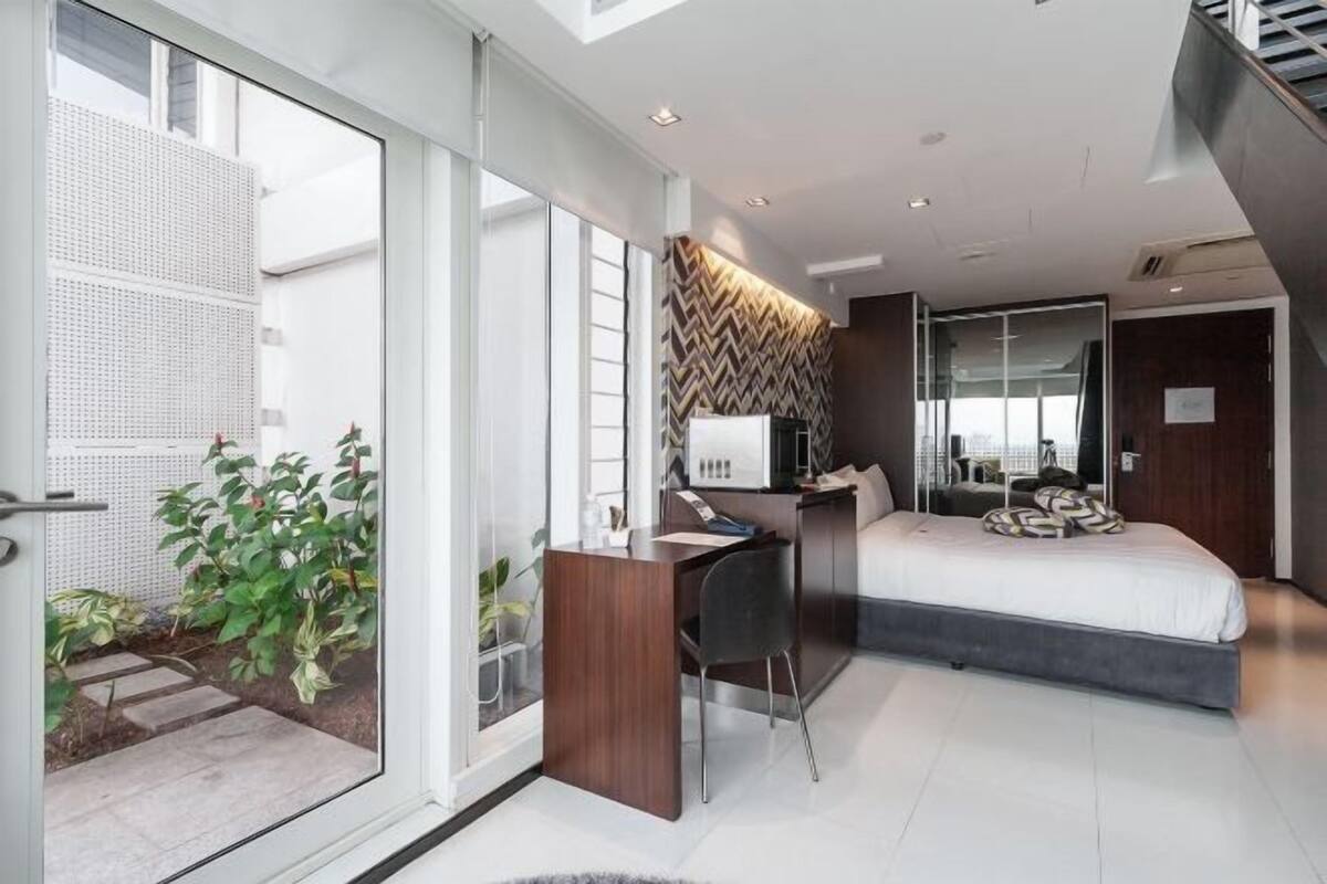 Une chambre moderne avec un bureau, un lit et de grandes fenêtres.