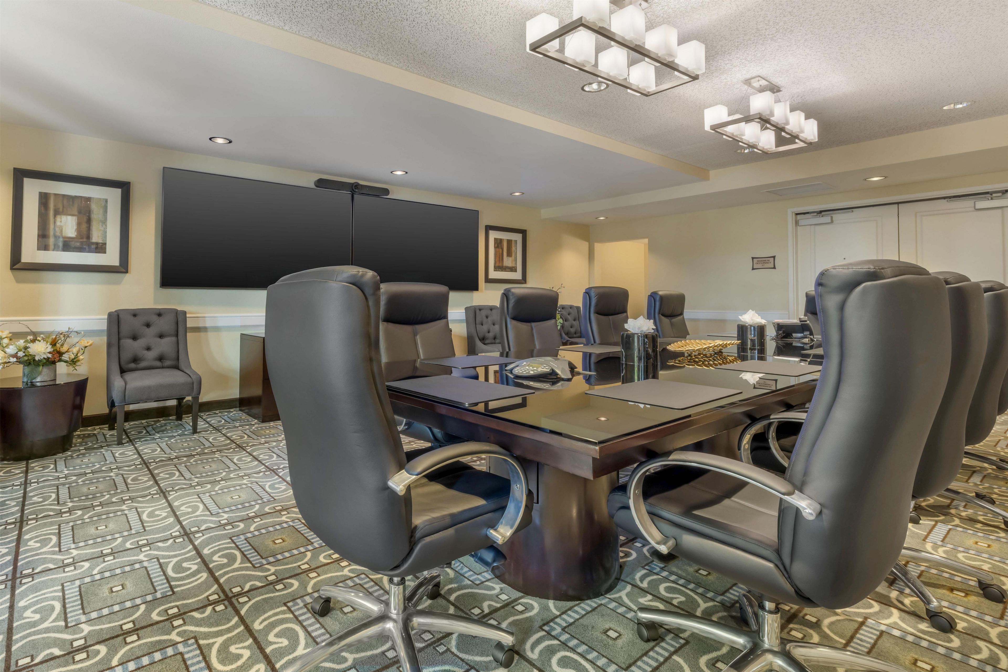 A conference room with a large table, multiple chairs, a projector screen, and a carpeted floor.