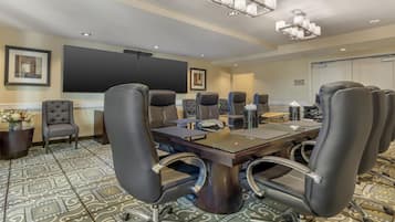 A conference room with a large table, multiple chairs, a projector screen, and a carpeted floor.