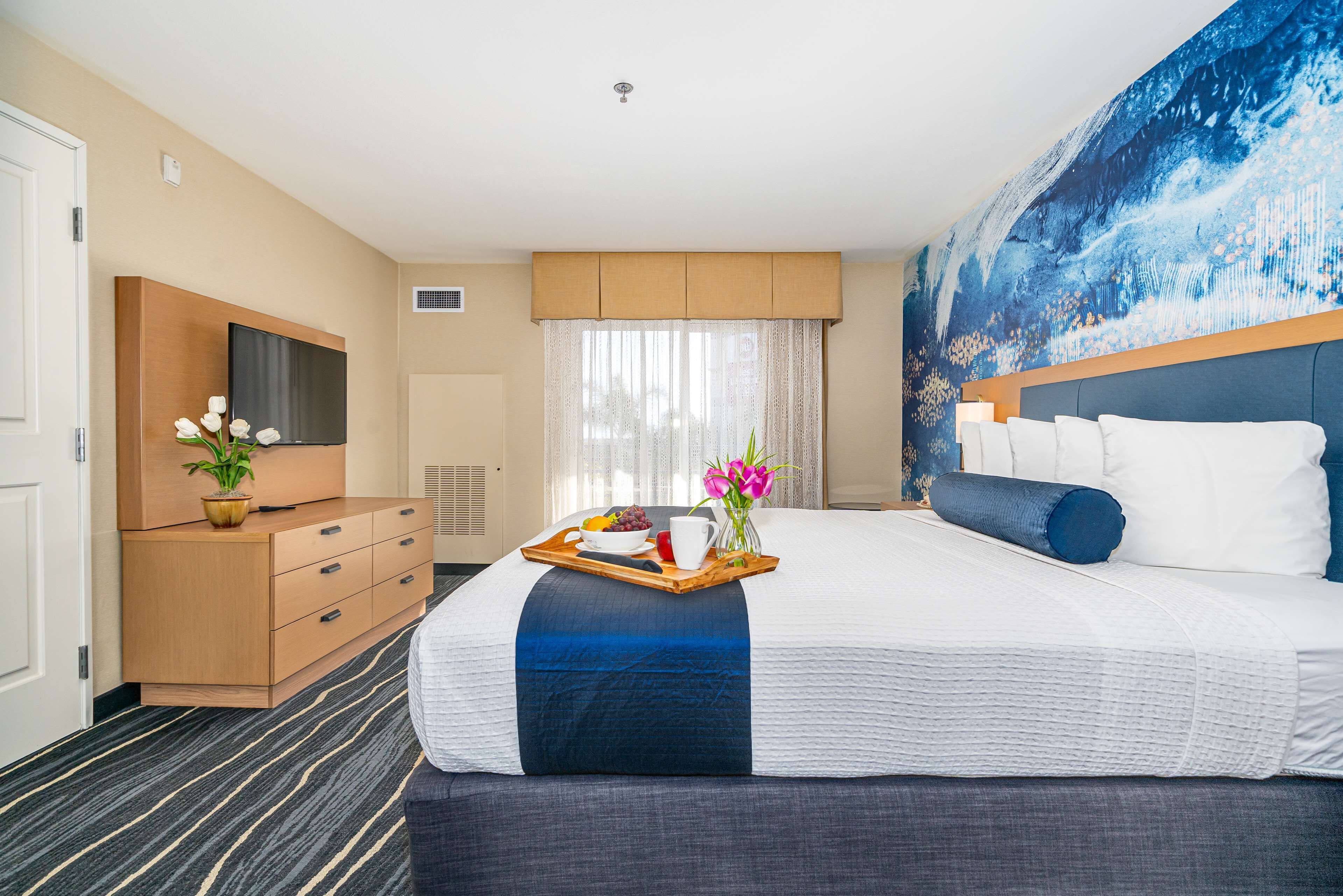 A hotel room with a large bed, a wooden dresser, a flat-screen TV, and a painting on the wall.