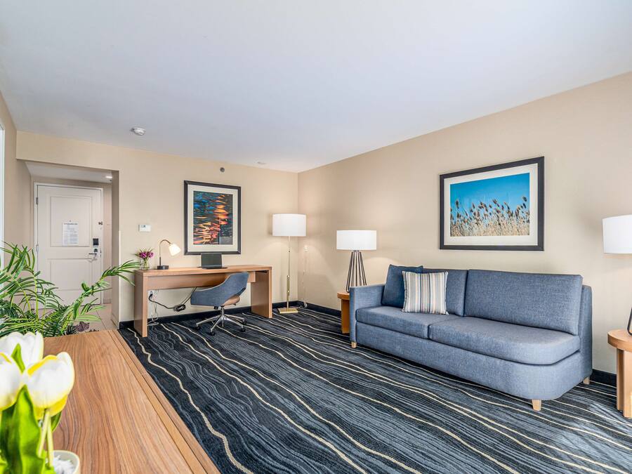 A hotel room with a desk, a sofa, a TV, and a large window.