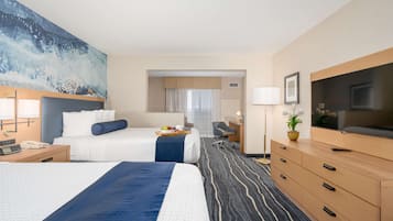 A hotel room with two beds, a desk, a TV, and a painting on the wall.