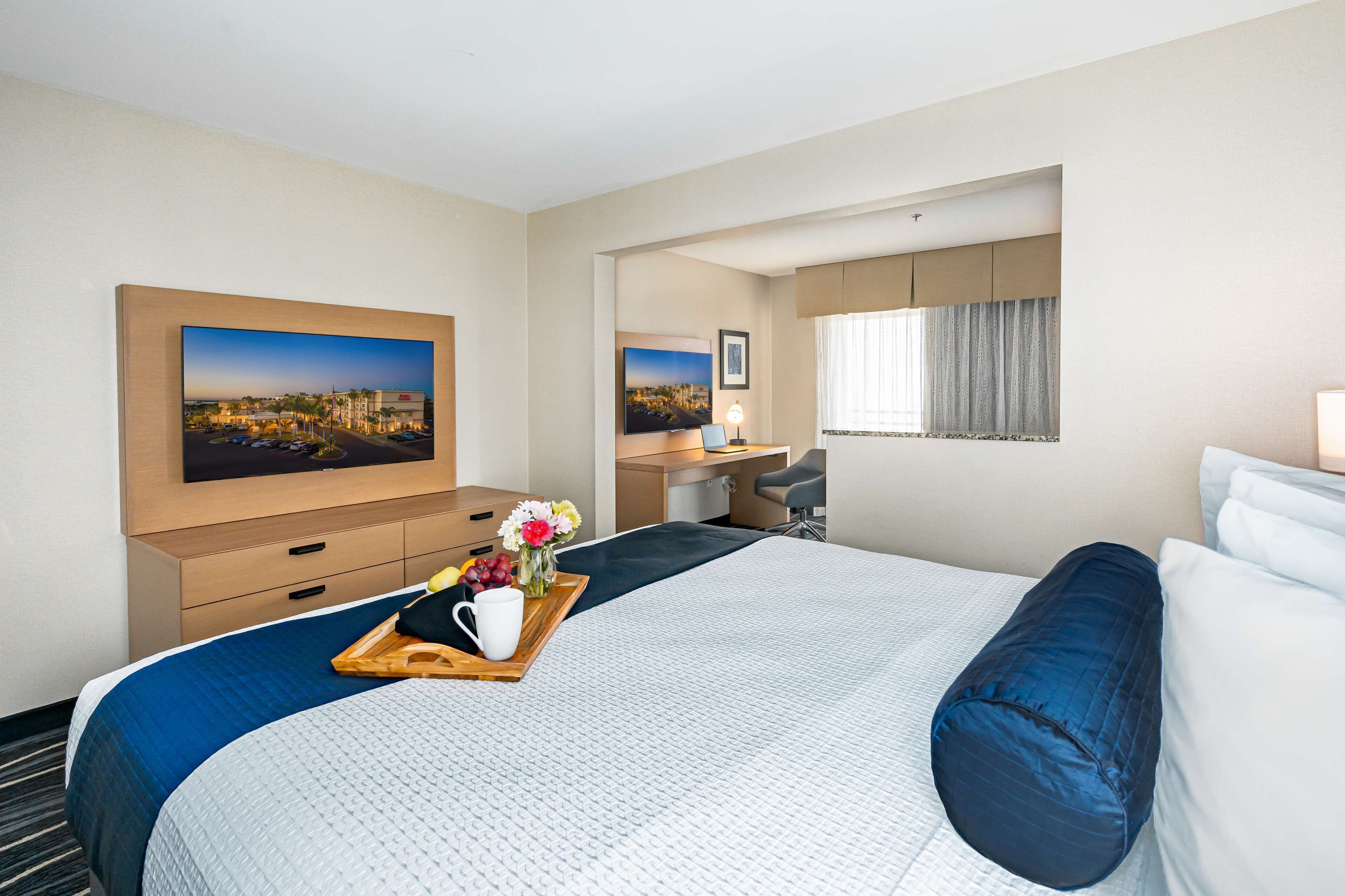 A hotel room with a large bed, a desk, and a television displaying a cityscape.